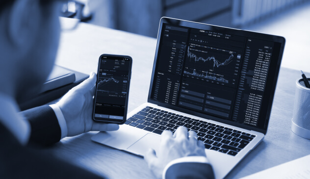 Person viewing financial trading charts on laptop and phone